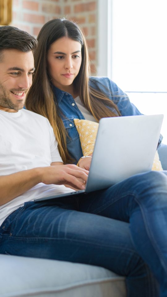 a man and woman sitting on a couch with a laptop at The Woodview